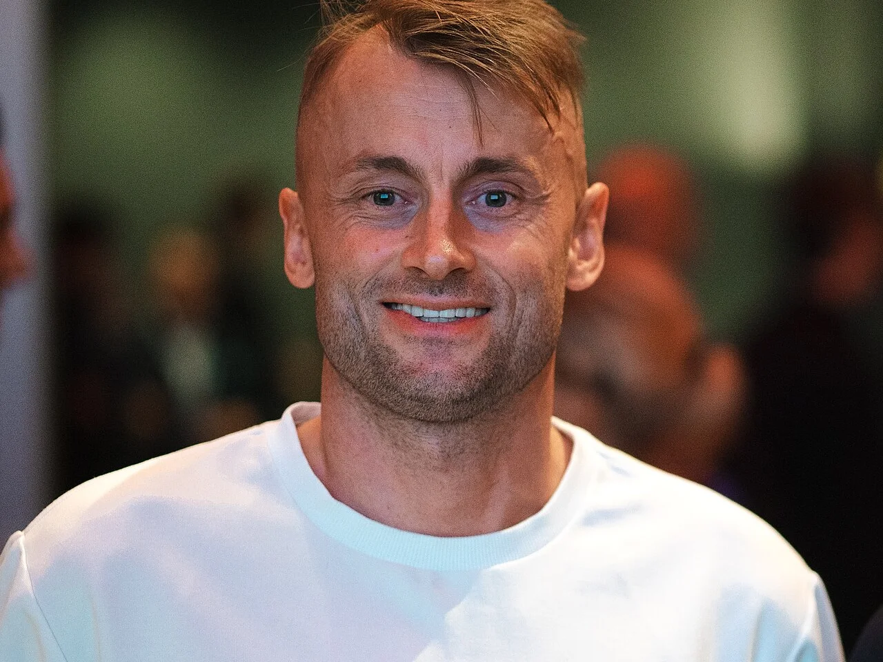 Petter Northug ler mot kameran i vit tröja, fotograferad 2025